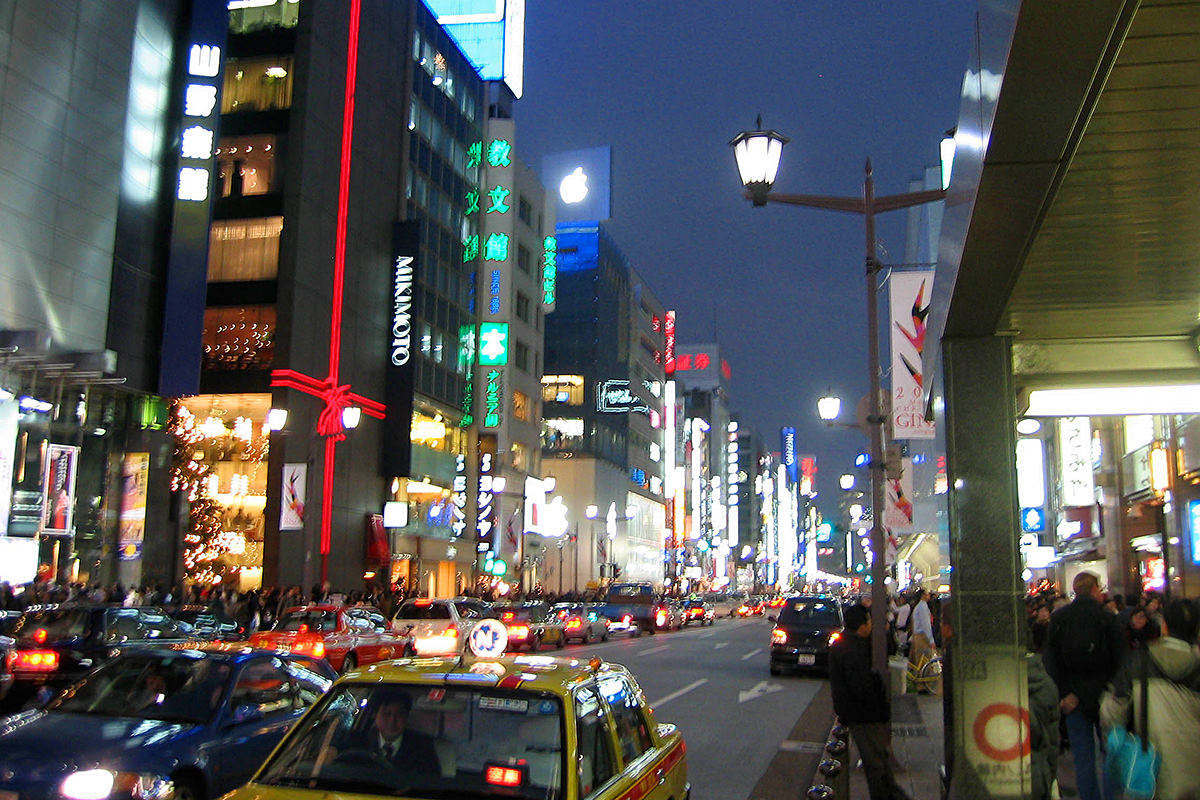 Looking down The Ginza at night with all the buildings lit up and a lighted Apple logo on top of the Apple Store Tokyo.