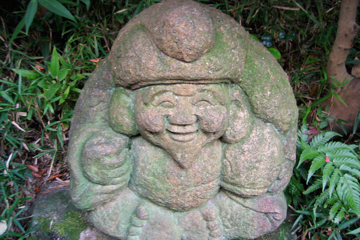 A stone carving of a smiling Buddha in a park at Chinzan-so.