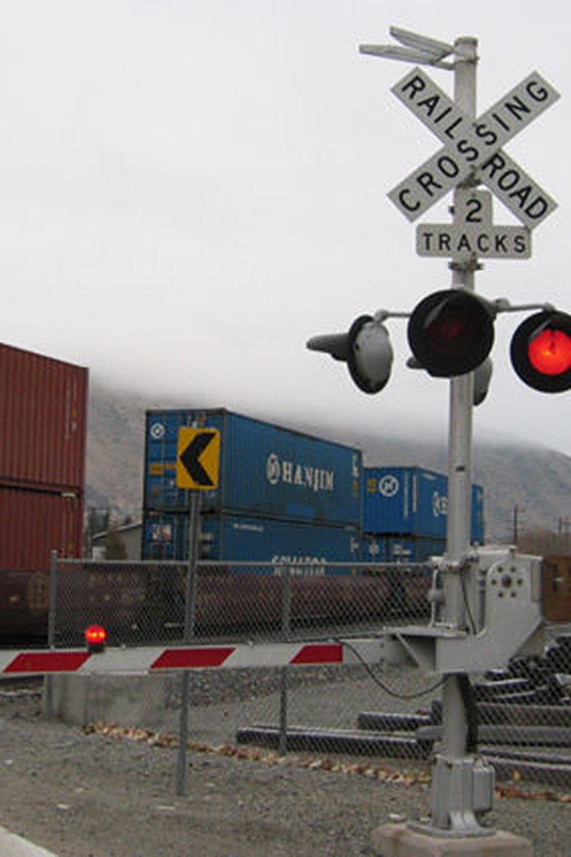 A railroad crossing on a cloudy winter day with the cross arm down to block traffic and a train passing behind it.