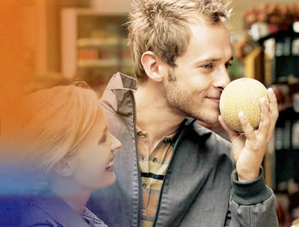 Guy smelling a cantaloupe melon at a market stall.