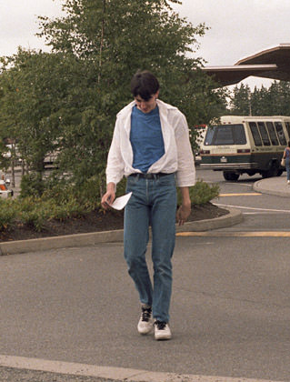 Old photo of Dave avoiding the camera while wearing too-tight jeans, a blue T-shirt, and a flowing white dress shirt tucked into his jeans which is opened to the navel.