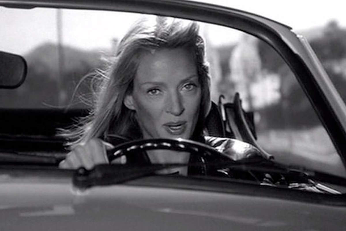 Kill Bill 2 Teaser Trailer frame in black and white of Uma Thurman as The Bride driving a car looking determined to KILL BILL.