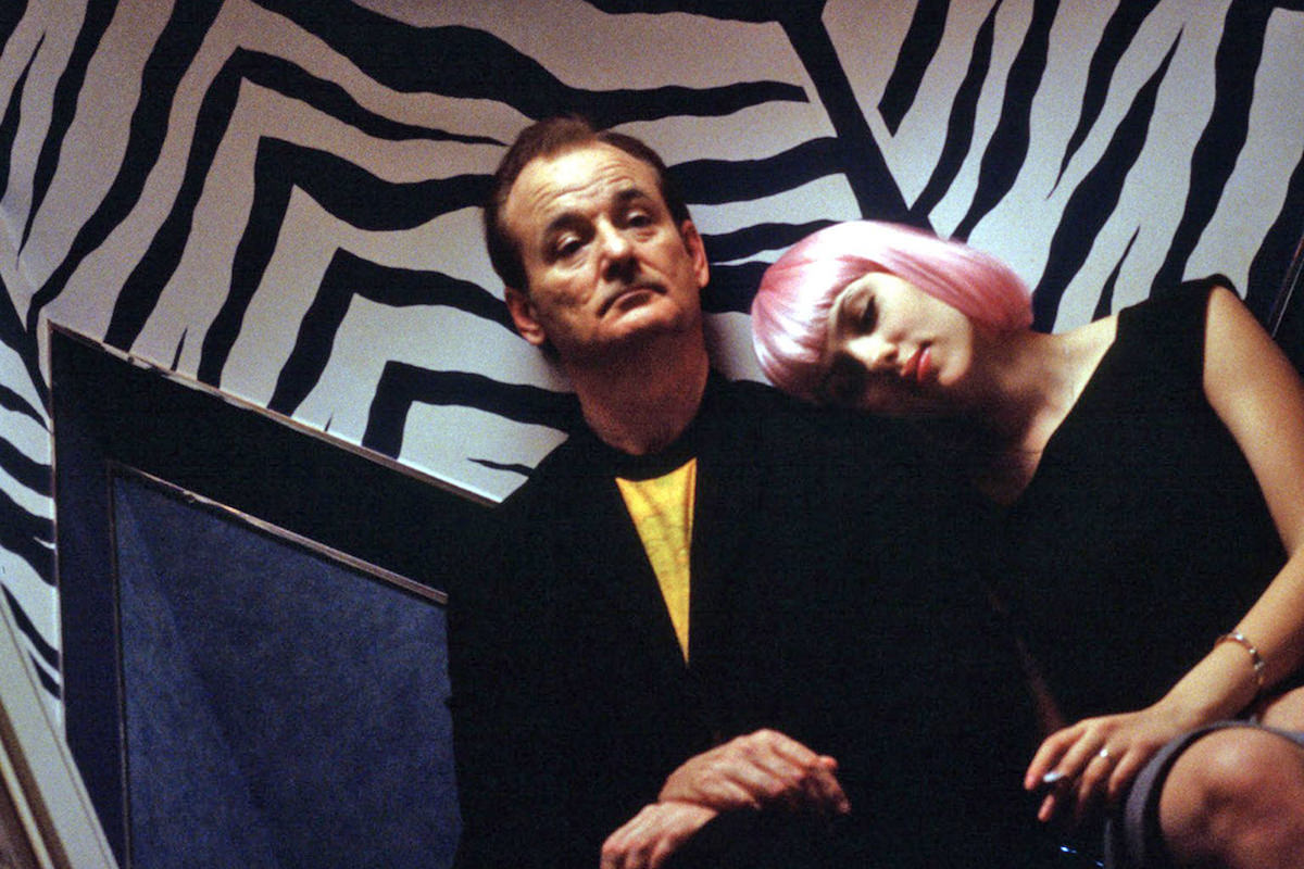 Bill Murray and Scarlett Johansson in a scene from Lost in Translation where they are sitting against a zebra-stripe wall looking tired.