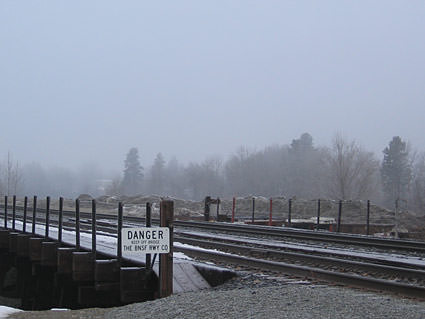 A fence with a DANGER! sign bordering some railroad tracks on a foggy day.