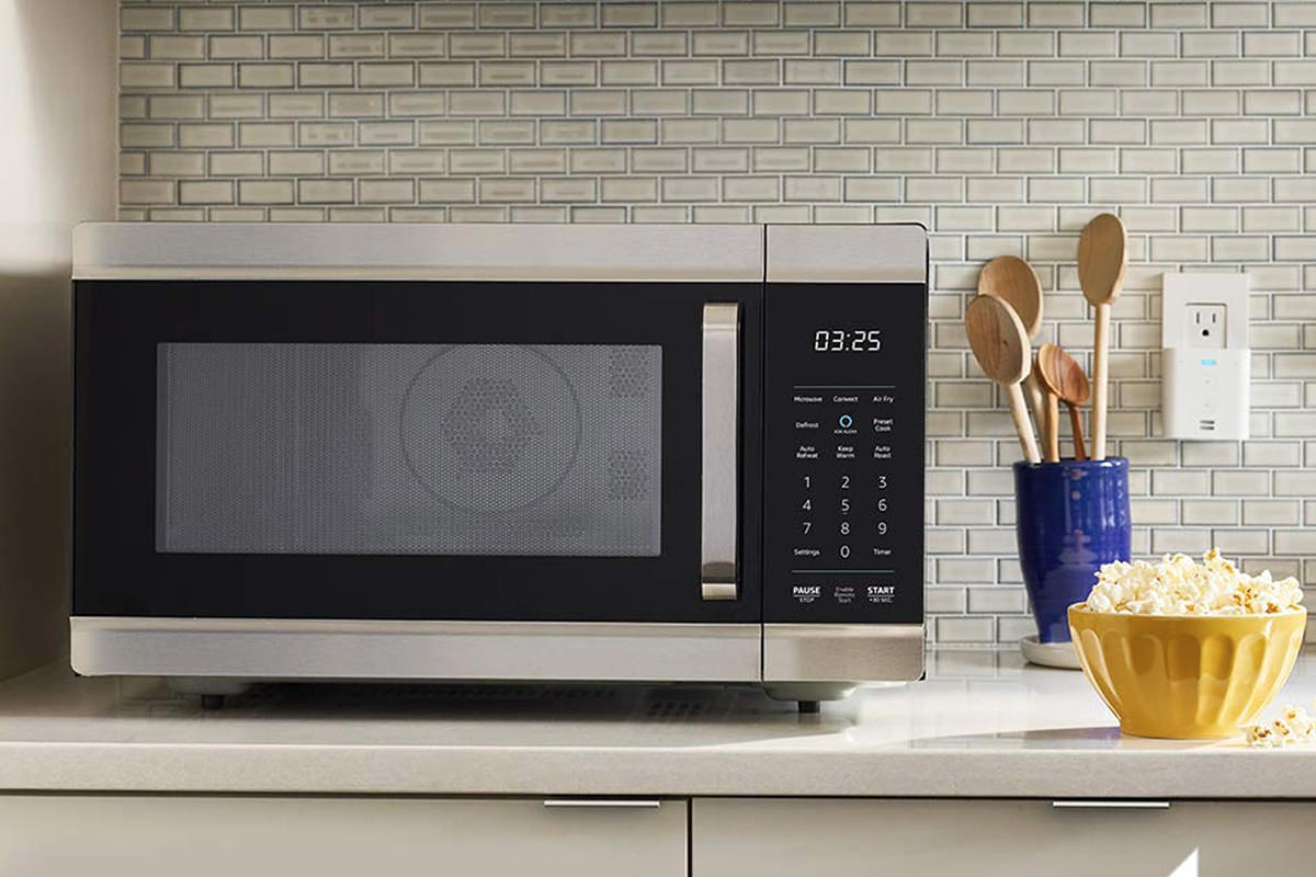 An Amazon Oven, looking much like a microwave, sitting on a kitchen counter next to a bowl of popcorn.