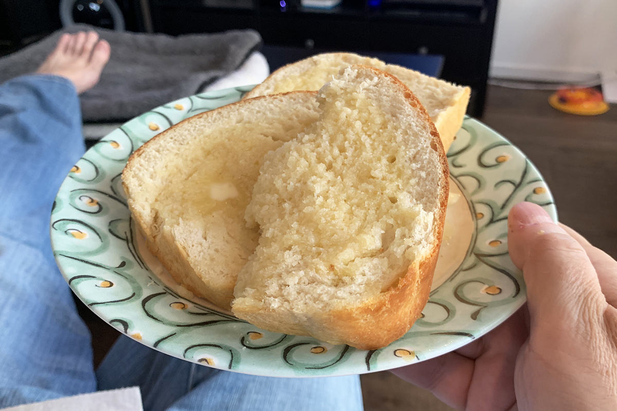 Three slices of freshly-baked bread with tons of butter stacked on a plate that I'm holding in my living room with one slice half-eaten.