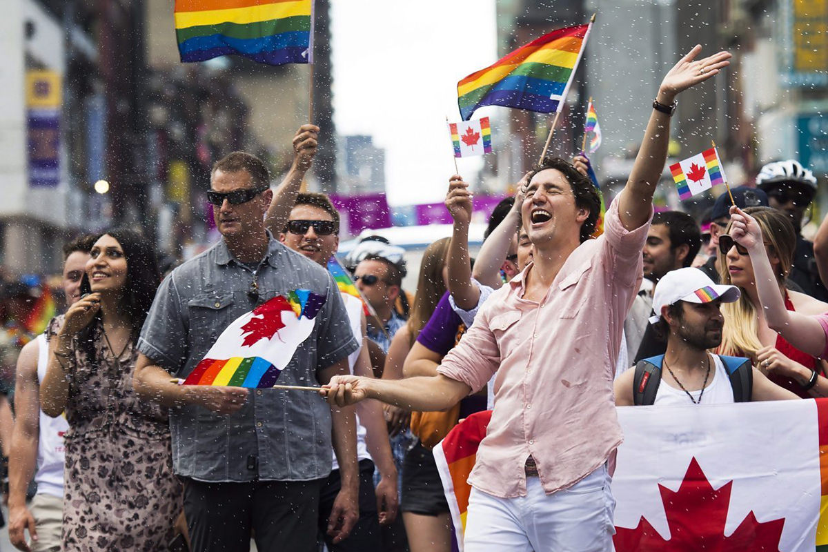 Prime Minister Justin Trudeau marching in a Pride parade with rainbow flags, fun, and confetti.