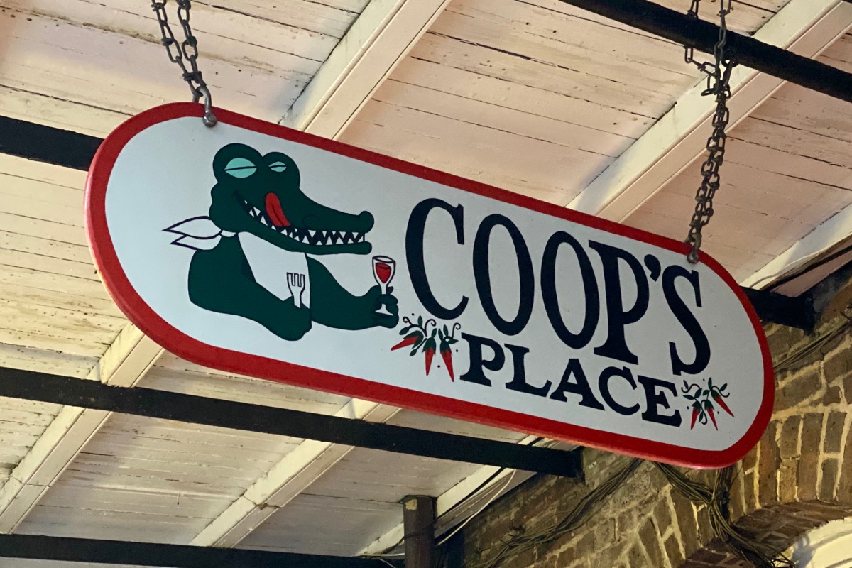 The sign for Coop’s Place which features an Alligator drinking a glass of wine and licking his lips.