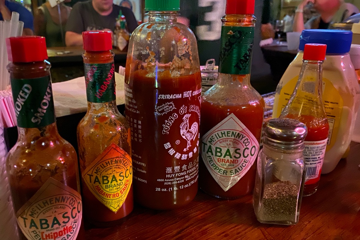 A bar top with four kids of hot sauce and other condiments, including a bottle of generic mayonnaise.