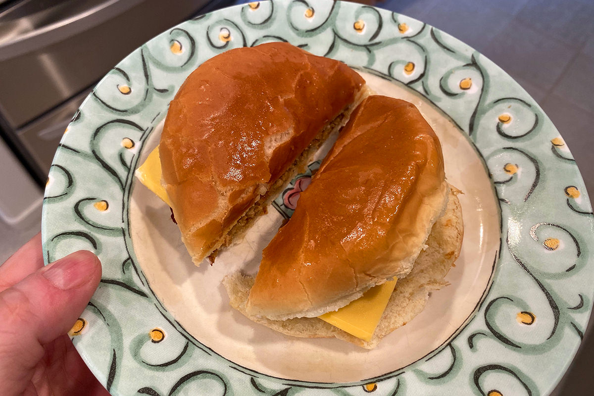My morning breakfast hamburger sitting on a plate, cut in half.