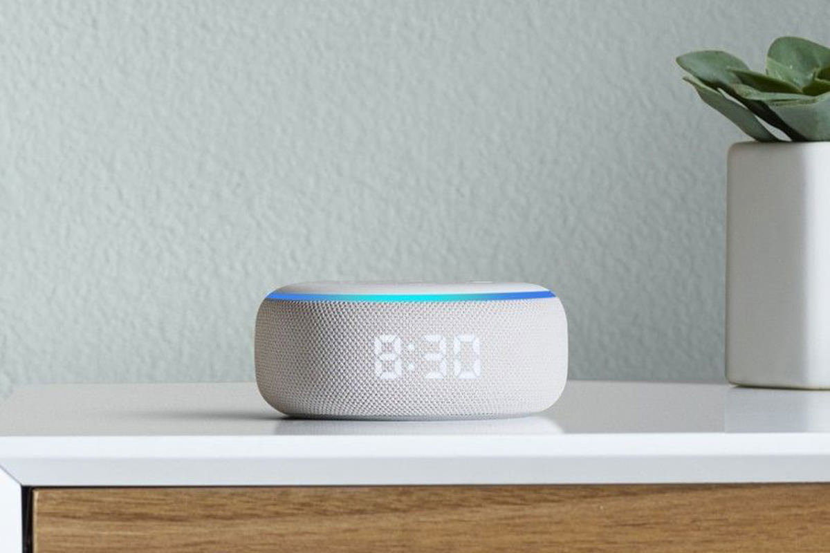 An Echo Dot sitting on a corner table with the time serenely glowing through the fabric of the speaker cover the circles the hockey-puck-shaped device.