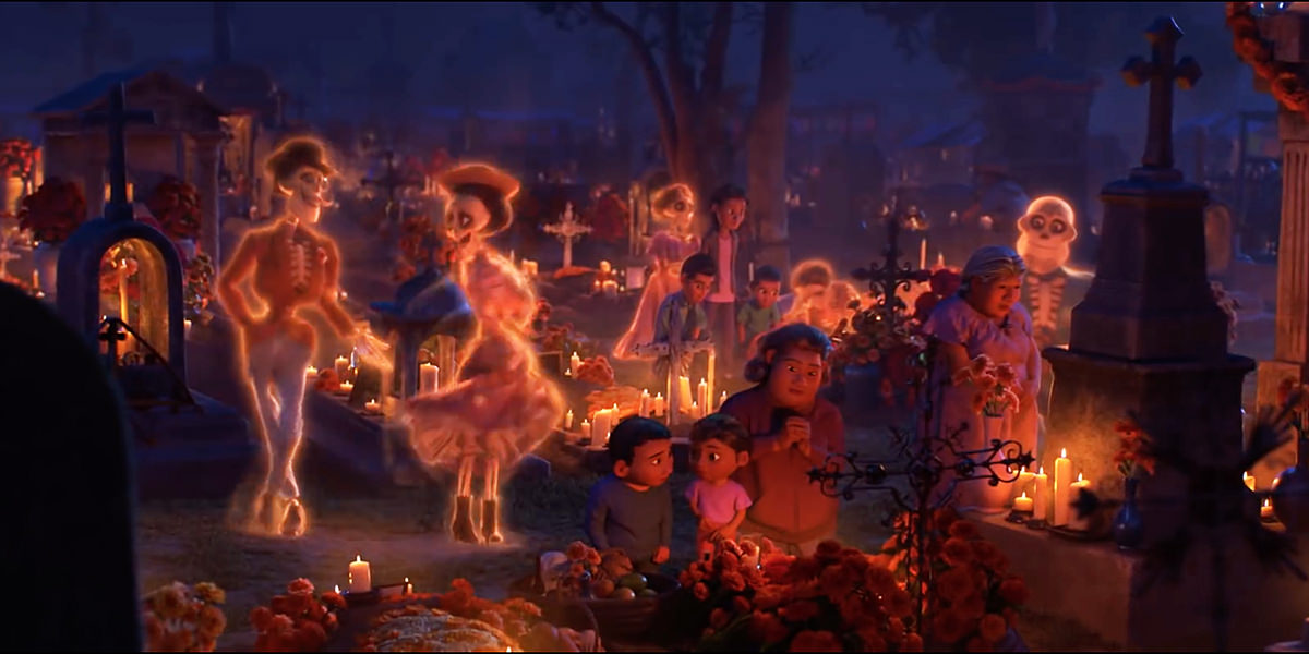 A frame from the animated masterpiece COCO from Disney Pixar showing skeletal spirits visiting a decorated cemetery while people are praying at a gravesite in the foreground.