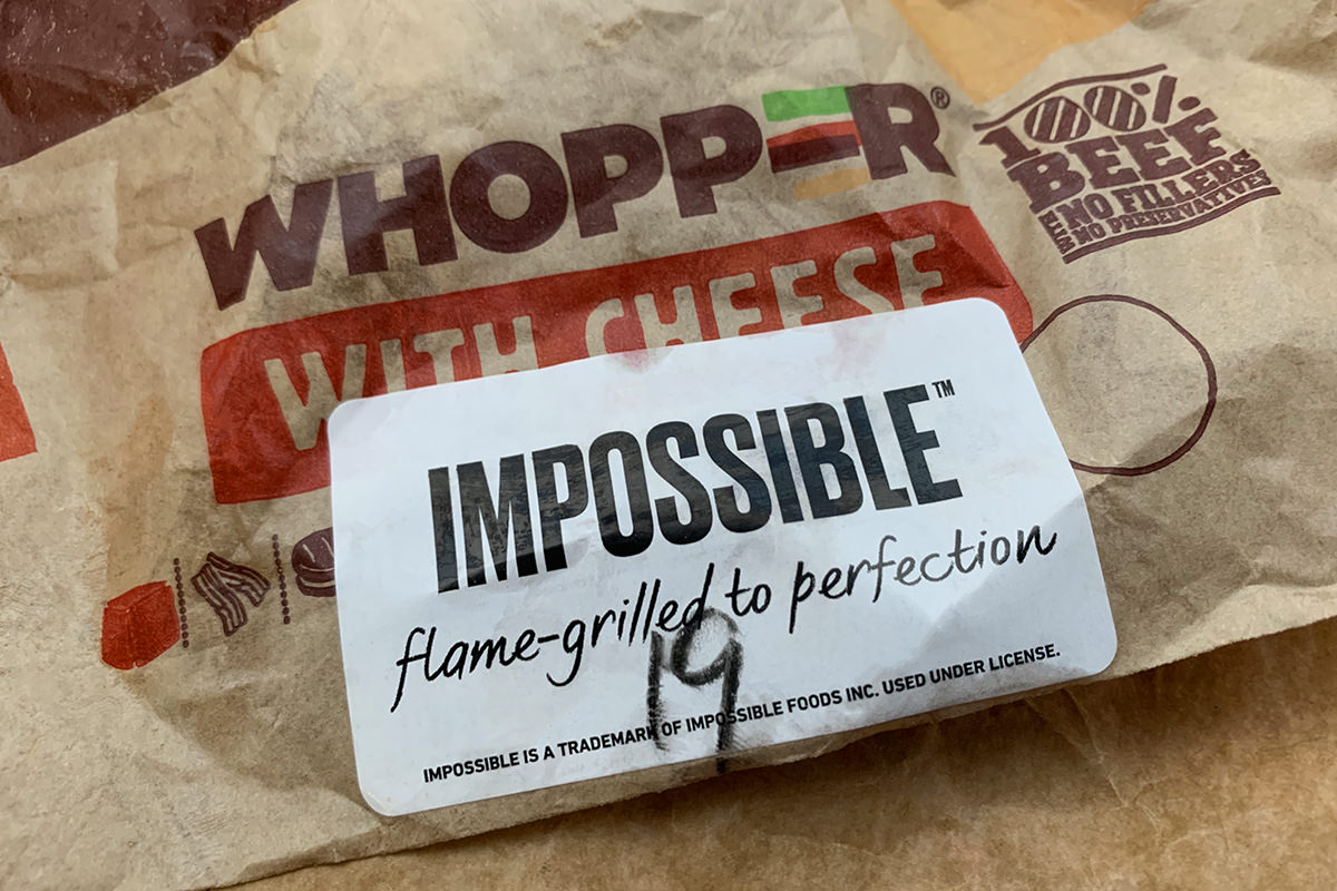 A Burger King Whopper hamburger in a wrapper with an Impossible Whopper sticker on the front.