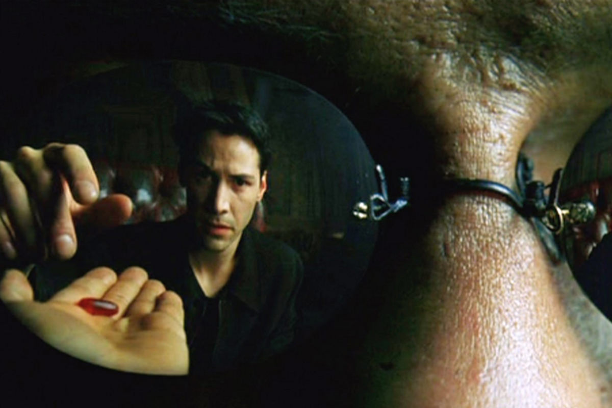 Neo is reflected in Morpheus' glasses taking the red pill in a scene from The Matrix.