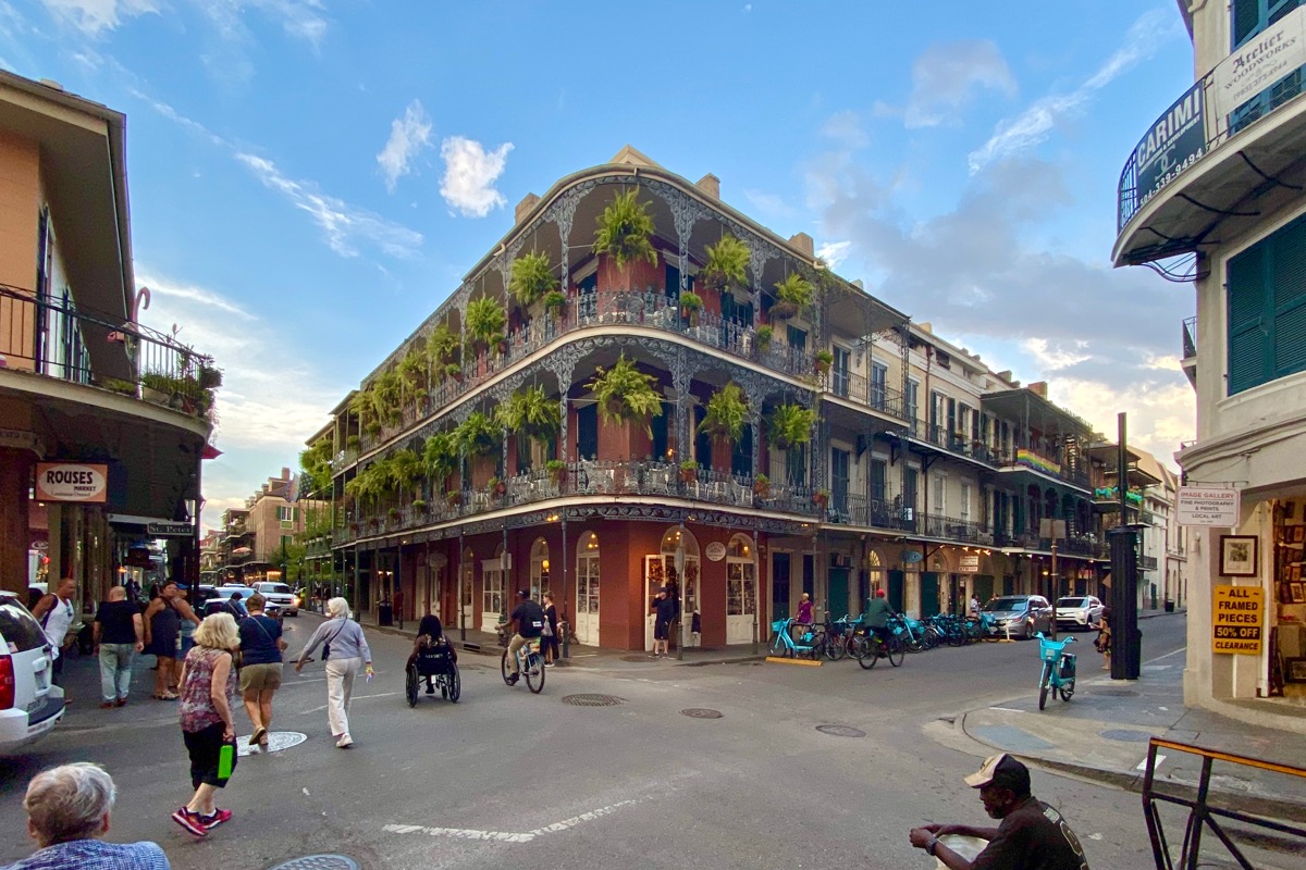 This time a wide-angle photo of a beautiful New Orleans building with wrought iron railings and massive ferns hanging on the balconies... with people in the street in front of and around it.