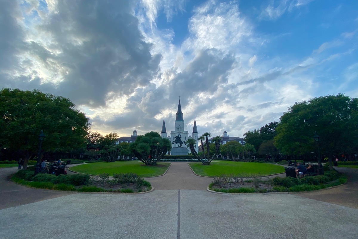 A wide-angle shot of St. Louis Cathedral at dusk as seen through Jackson Square with its beautifully manicured lawn and greenery. A statue of Jackson on a horse is in the middle of the park.