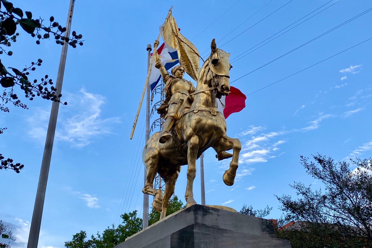 A beautiful gold-covered statue of Joan of Arc, which was a gift to New Orleans from the people of France. A French flag can be seen on a pole behind it.