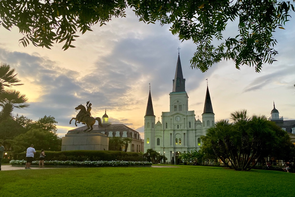 St. Louis Cathedral at dusk sitting behind Jackson Square with beautiful green lawns and a statue of Jackson on a horse in the middle.