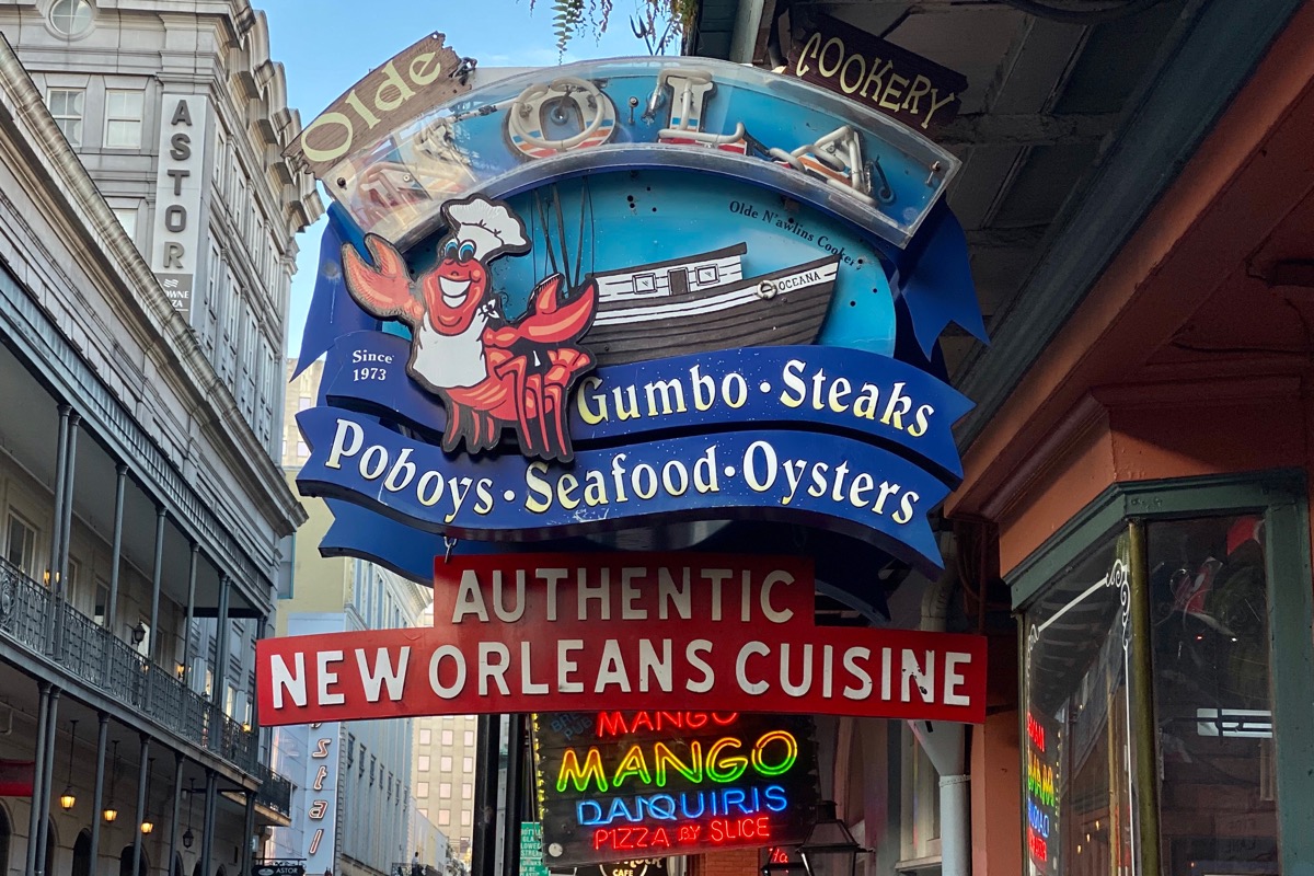 A sign for the Olde NOLA Cookery... with a crab chef and fishing boat plus the words AUTHENTIC NEW ORLEANS CUISINE underneath.