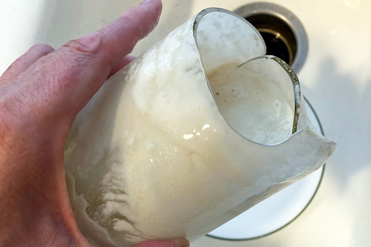 The Ball canning jar for my sourdough starter which has the bottom blown out and sourdough starter remnants in it being held over my sink.