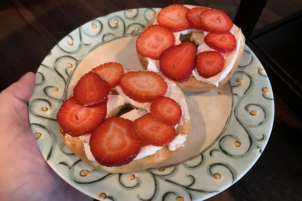 Strawberries sliced on top of a sliced and toasted bagel with cream cheese.