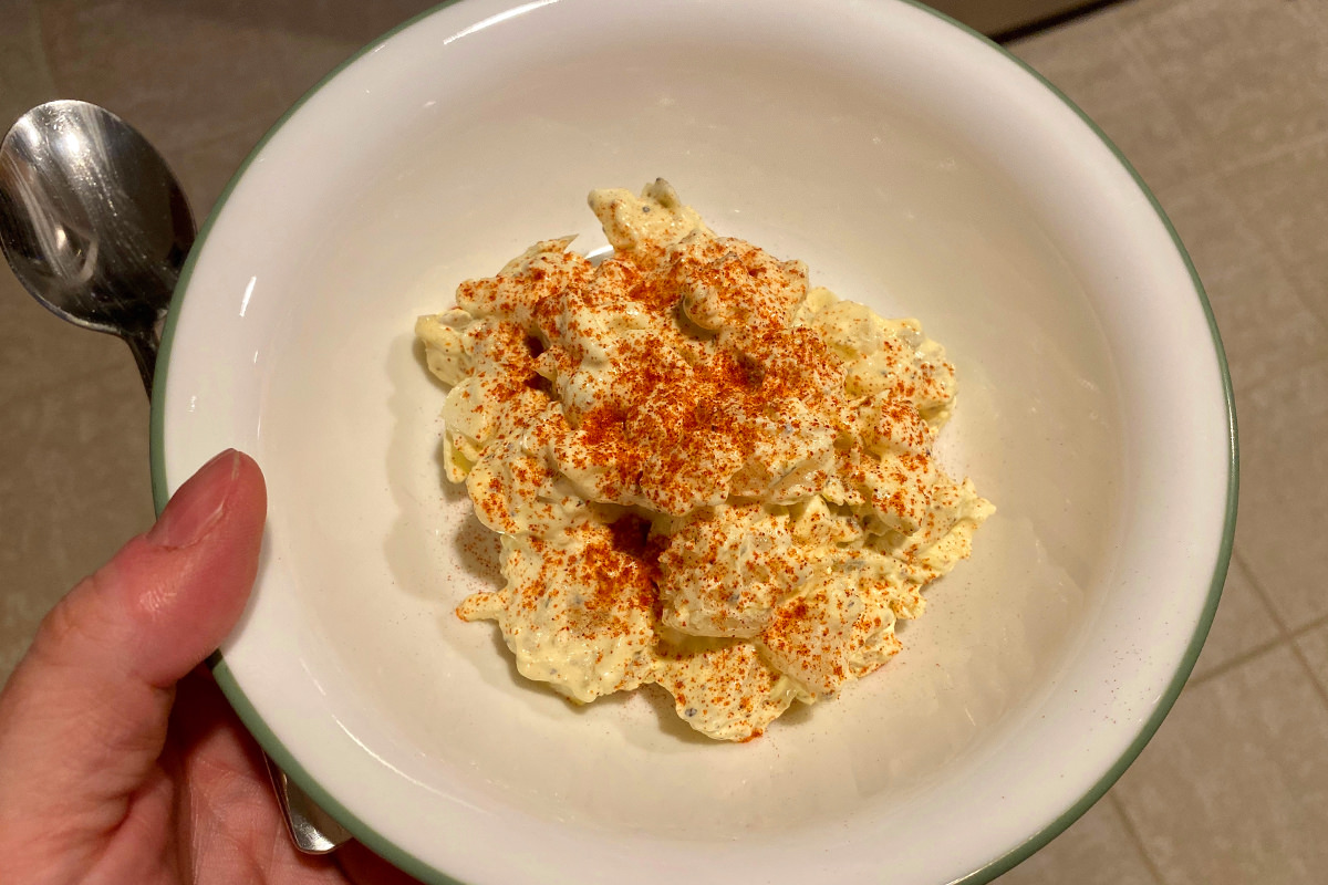 A beautiful scoop of my homemade potato salad with paprika on top sitting in a bowl and ready to be eaten.