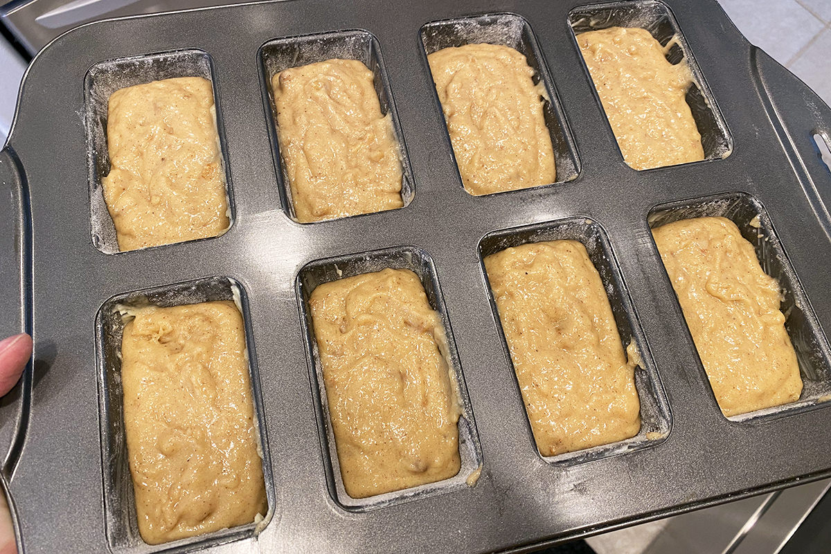 Raw applesauce bread poured into a tray with eight mini loaves stamped in it.