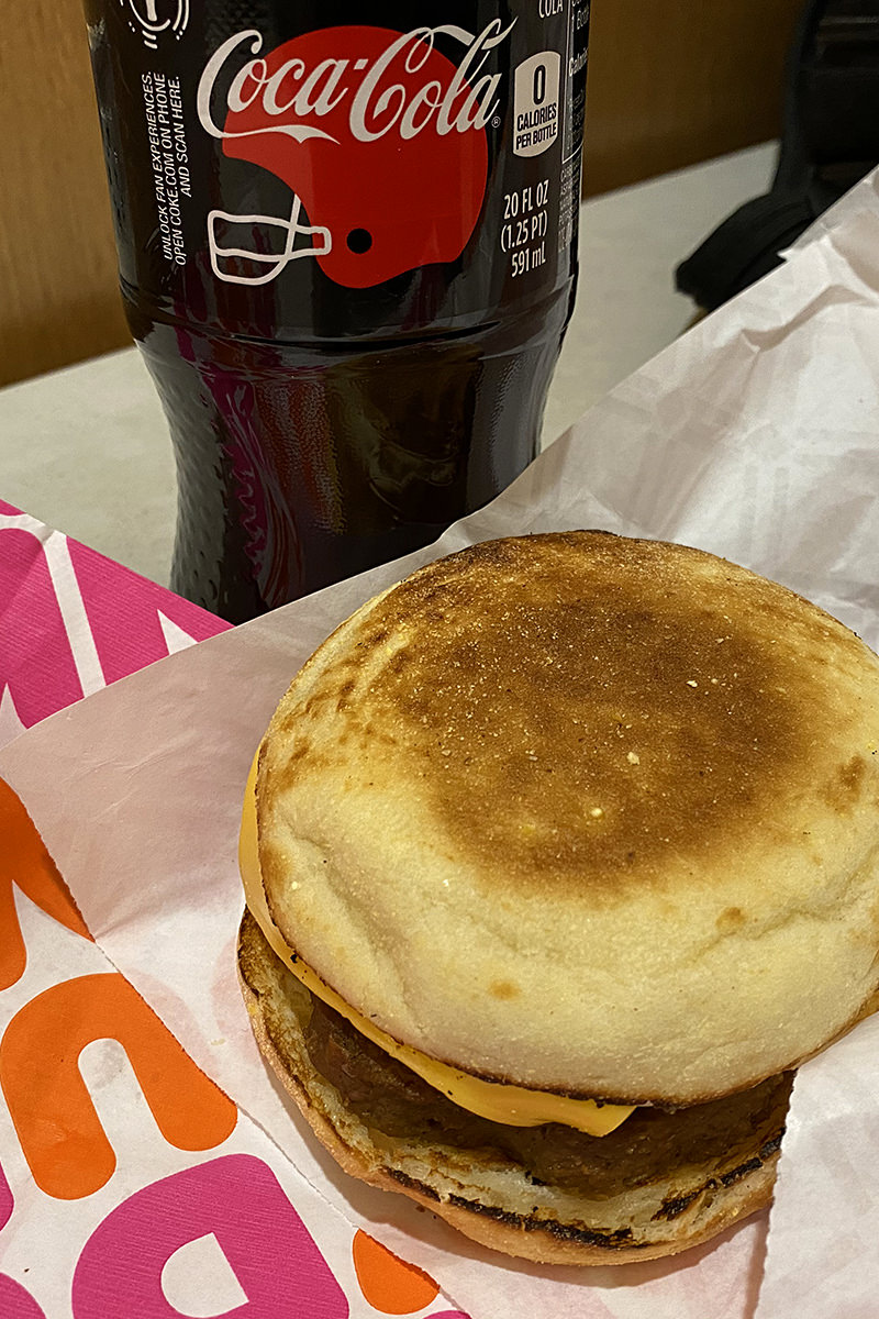 My Beyond Sausage breakfast sandwich sitting on a Dunkin Donuts wrapper in front of a bottle of Coke Zero.