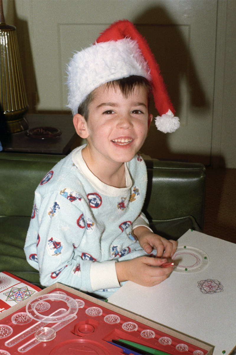 Young me playing with a Spirograph toy while wearing a Santa hat.