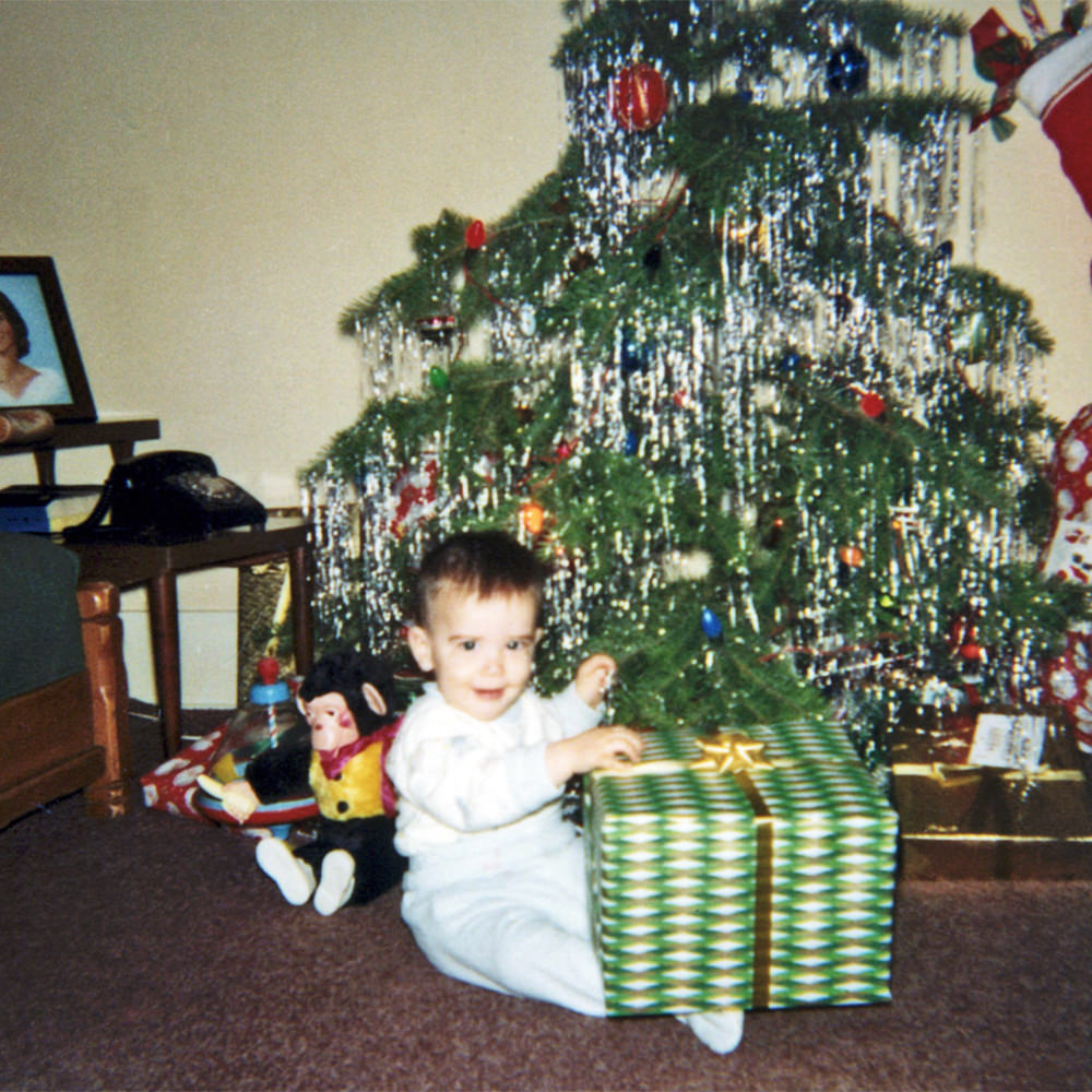 Baby me sitting in front of a Christmas tree with presents.