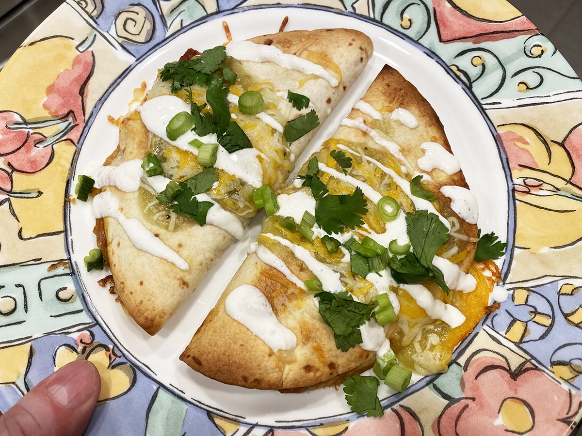 Two baked refried bean quesadillas topped with cheese, crema, cilantro, and green onions.