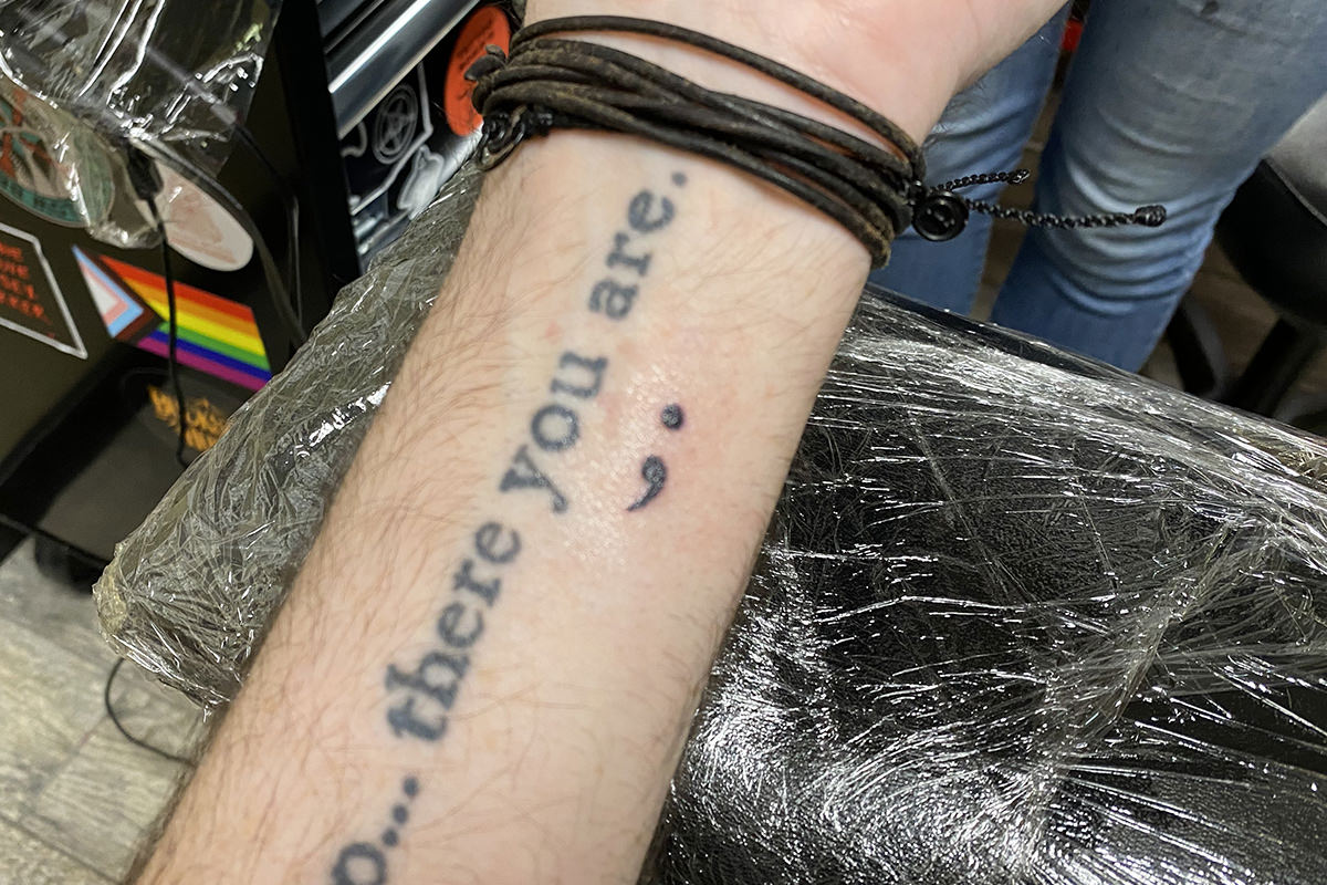 A tattoo of a semicolon inked under the word YOU in NO MATTER WHERE YOU GO, THERE YOU ARE that's on my arm.