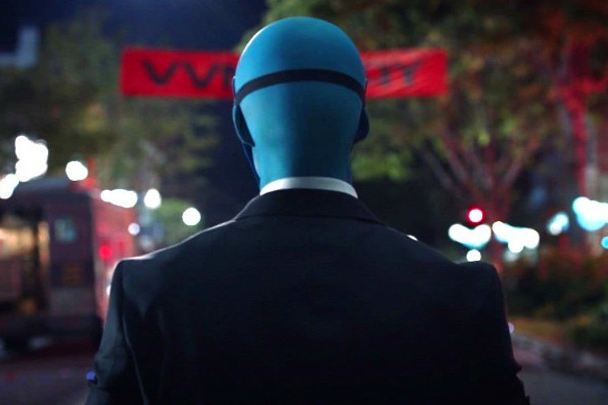 Dr. Manhattan walking through Vietnam with a mask on, his back towards us.