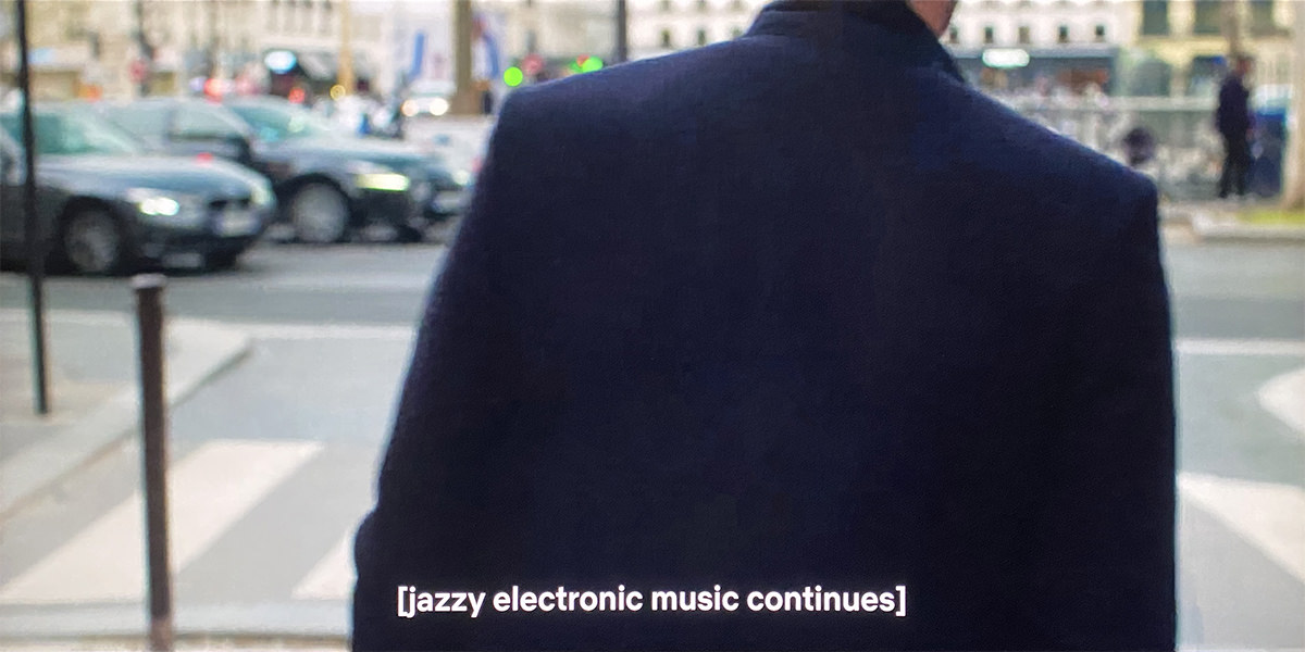 A man is walking away from the camera and the subtitles say JAZZY ELECTRONIC MUSIC CONTINUES.