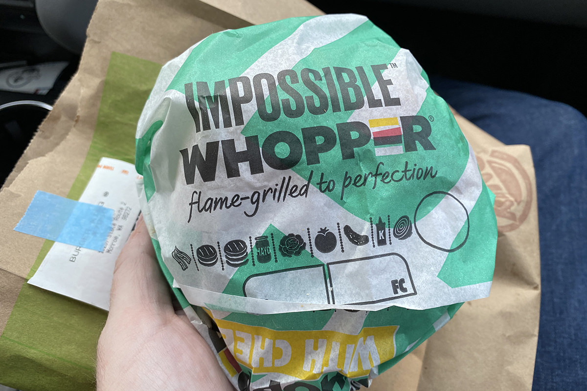 An Impossible Whopper still in its wrapper on top of a Burger King bag inside a car.