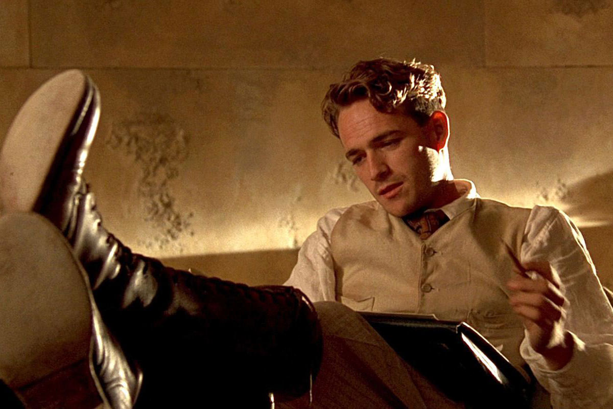 Luke Perry in The Fifth Element, leaning back in a chair while getting ready to tally Aziz, Light!