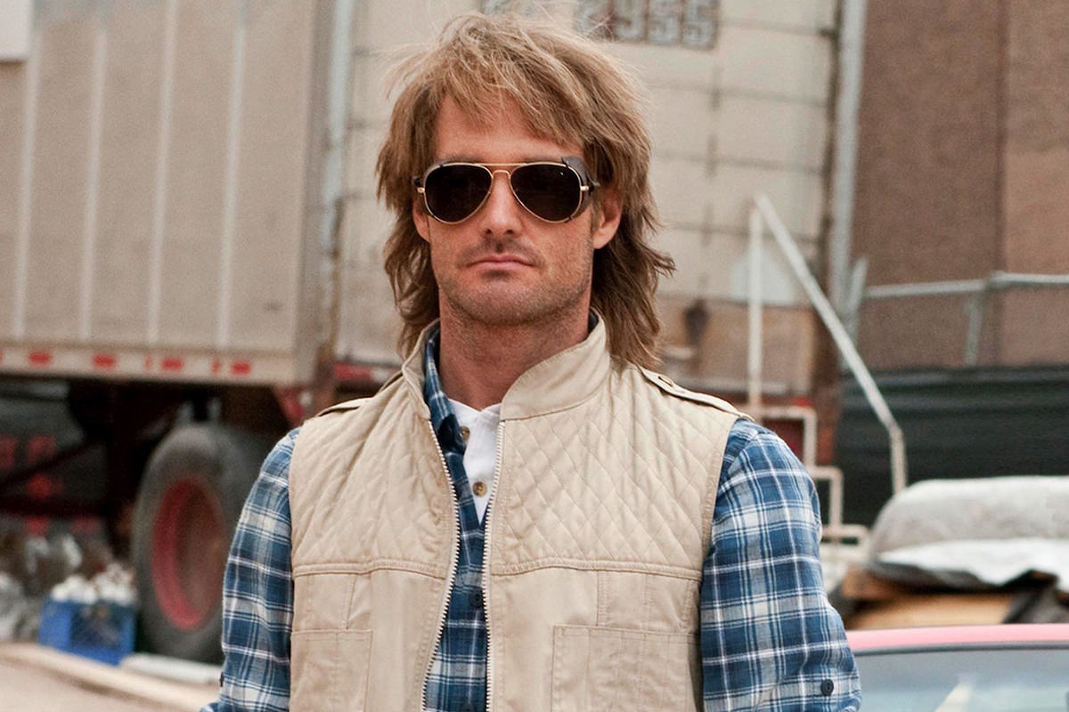 Will Forte as MacGruber wearing his trademark tan vest, plaid shirt, and sunglasses.