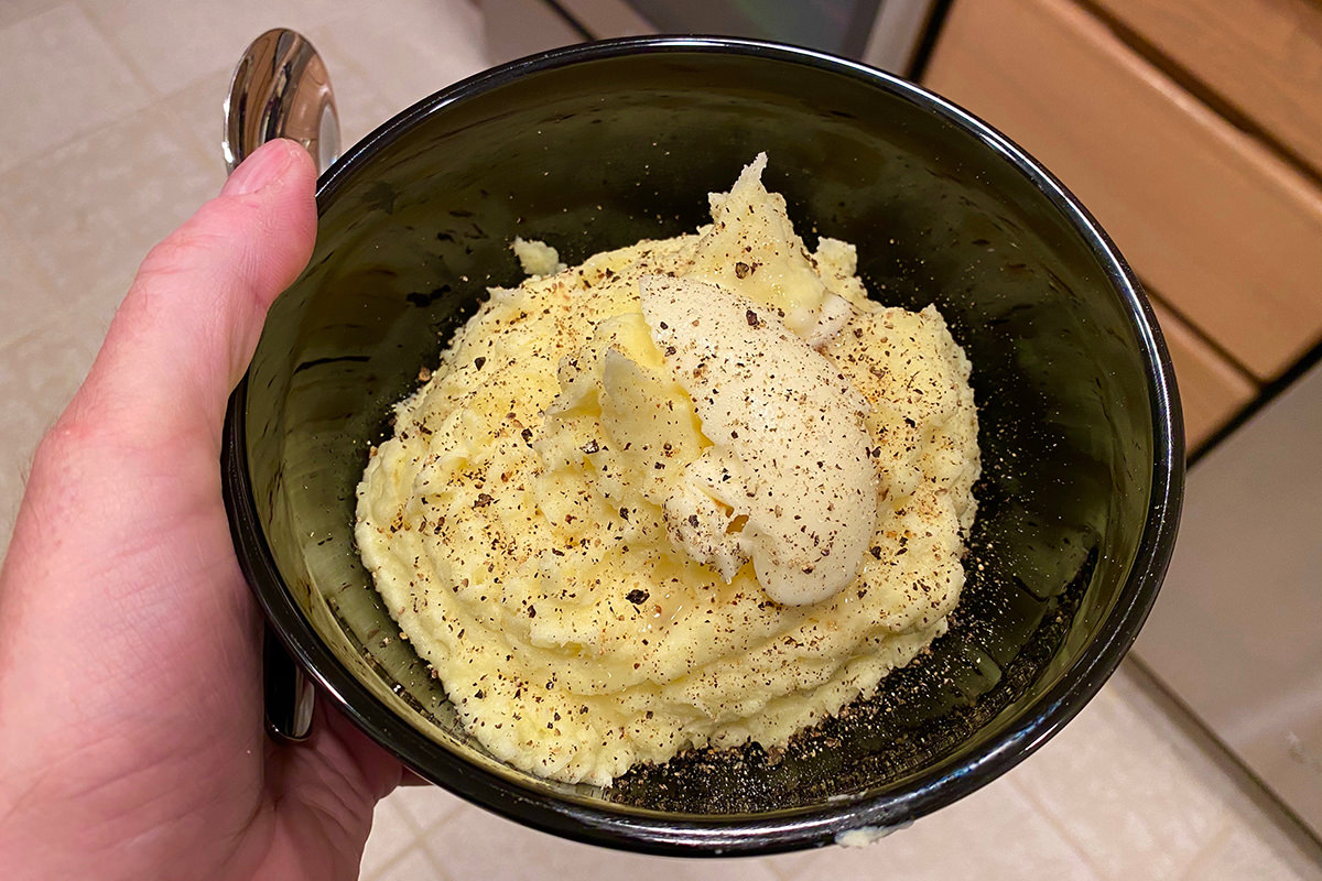 A beautiful black bowl in my hand with gorgeous, fluffy potatoes inside... covered in black pepper and butter!