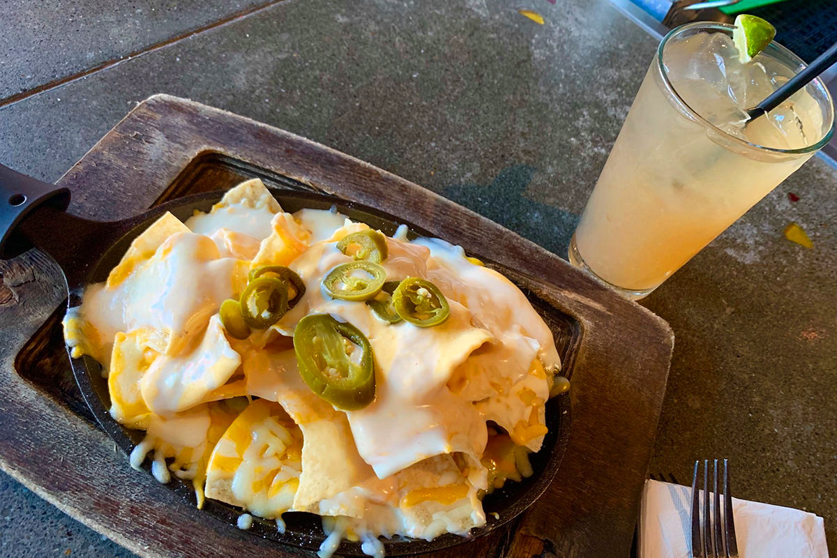 A plate of amazing-looking nachos sitting in front of a Long Island ice tea.