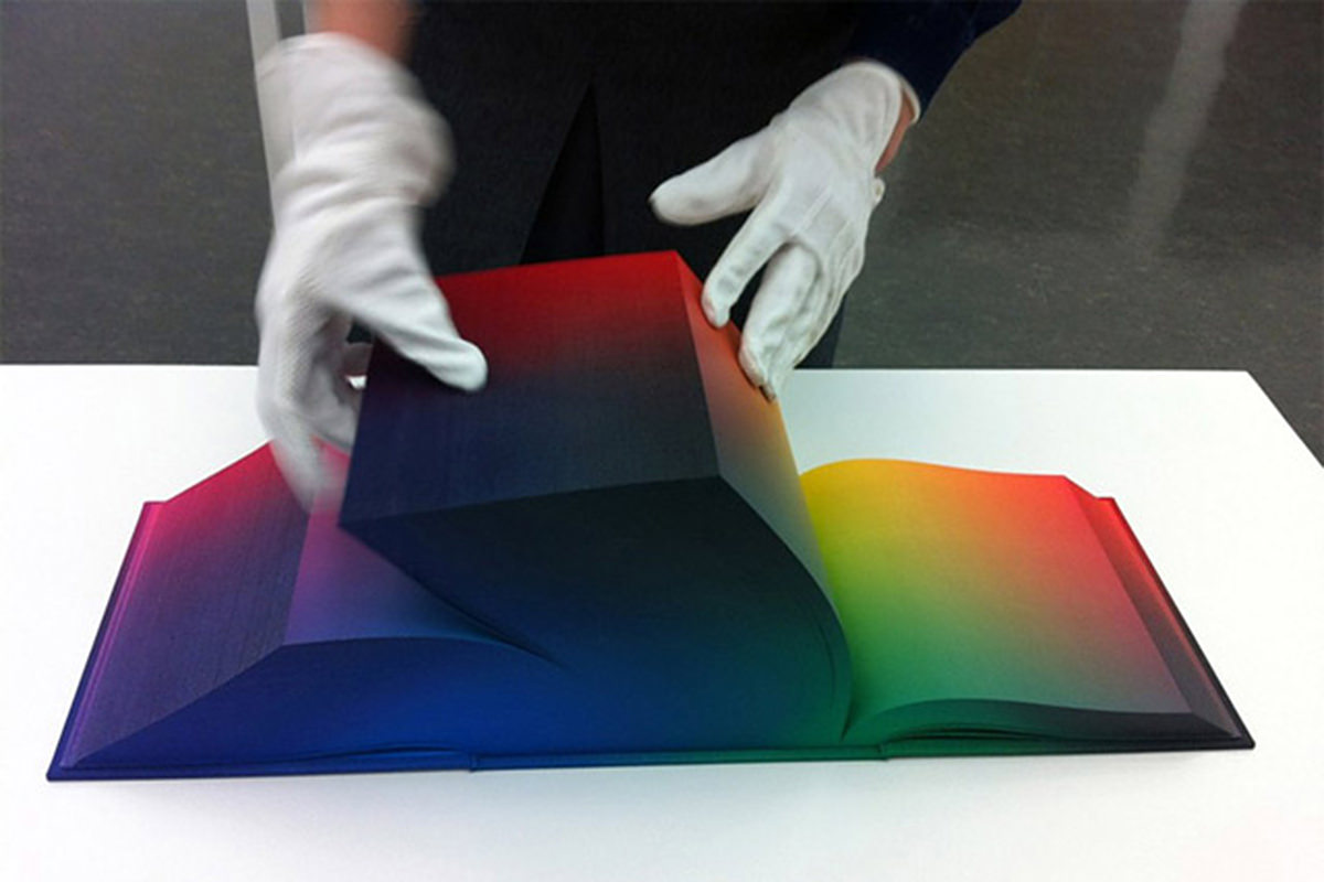 A person with white gloves turning the page of a massively thick volume of color pages in the RGB Color Atlas.