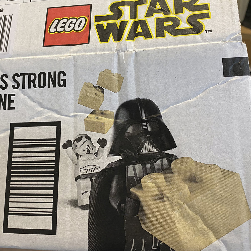 An Amazon box with LEGO Darth Vader using The Force to lift LEGO bricks over a LEGO Stormtrooper!