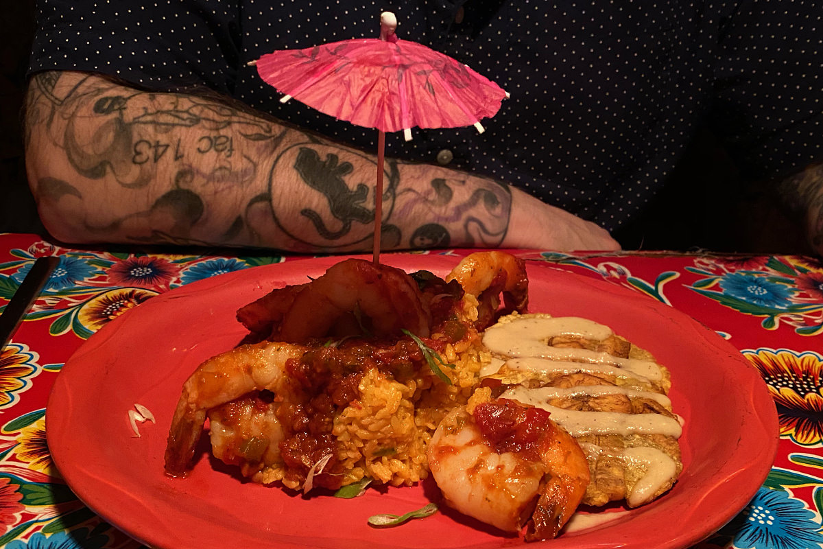 A close-up of Kyle's dinner with sauteed spricy shrimp on top of rice along with what looks like a yuca patty with cream sauce on top.