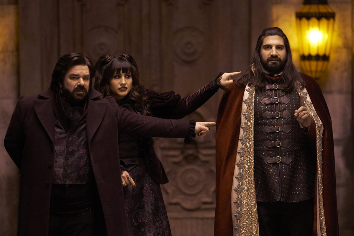 The TV cast for What We Do In The Shadows with two vampires pointing fingers at a third vampire