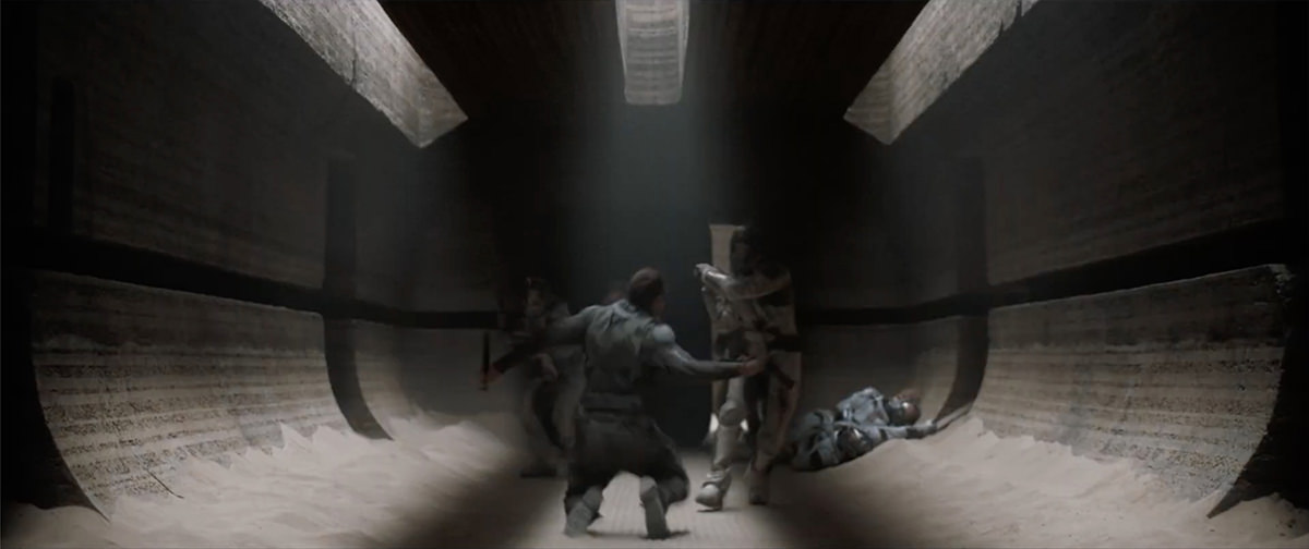 A large hallway in shadow with a fight happening in the middle, sand piled on the floor.