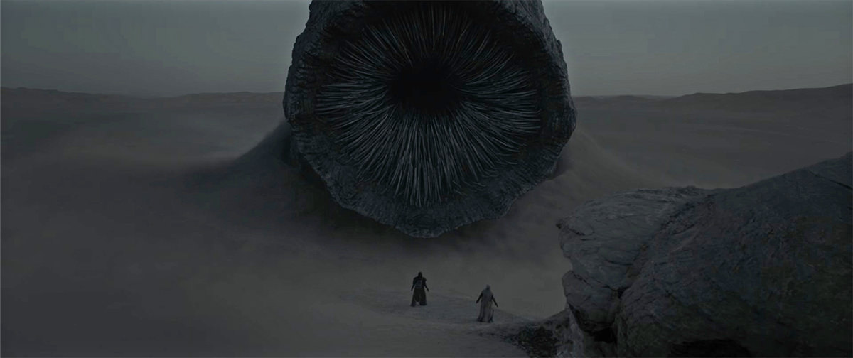 A massive sandworm approaches figures in the dessert... thousands of teeth crowding its maw.