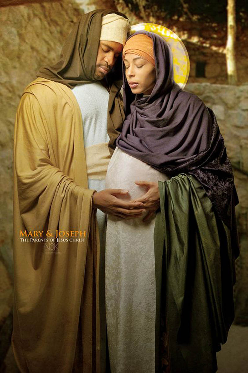 A pregnant Mary stands with a halo behind her head as Joseph lovingly touches her belly as photographed by James Lewis..