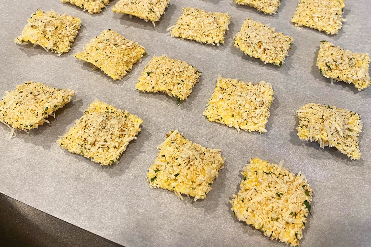 Dipped and battered raviolis resting on a baking sheet.