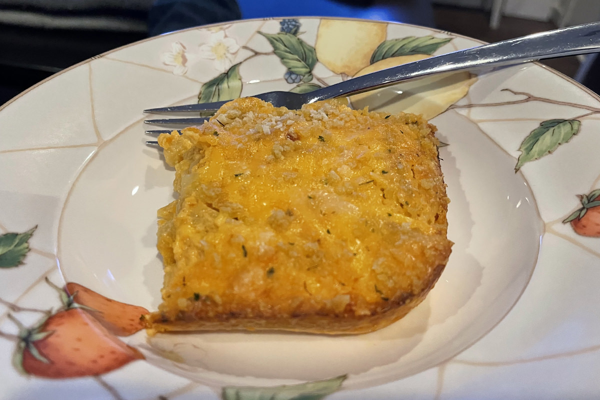 A baked Macaroni and Cheese on a plate. The glow of a television is in the background.