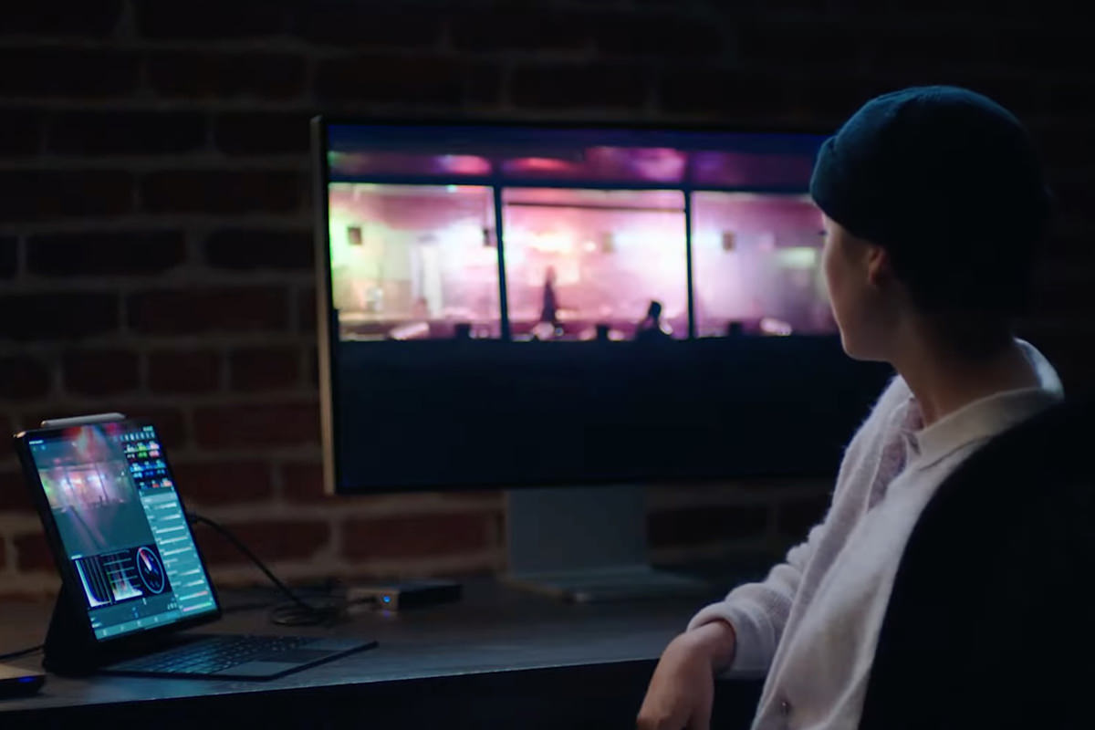 A guy editing video while looking at a massive external display connected to his iPad... the Mac is a beautiful yellow color.