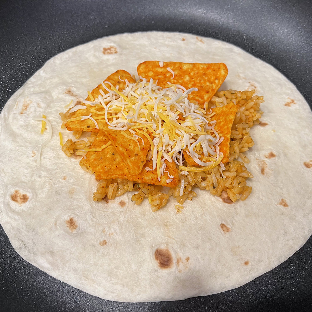 A tortilla in a pan with rice, Doritos, and cheese.